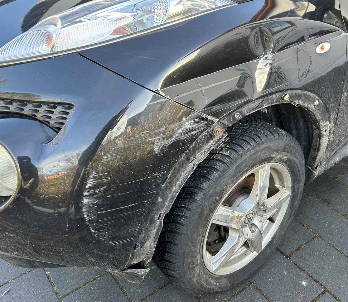 Vordere Fahrzeugecke mit gelöstem Stoßfänger und beschädigtem Radlauf